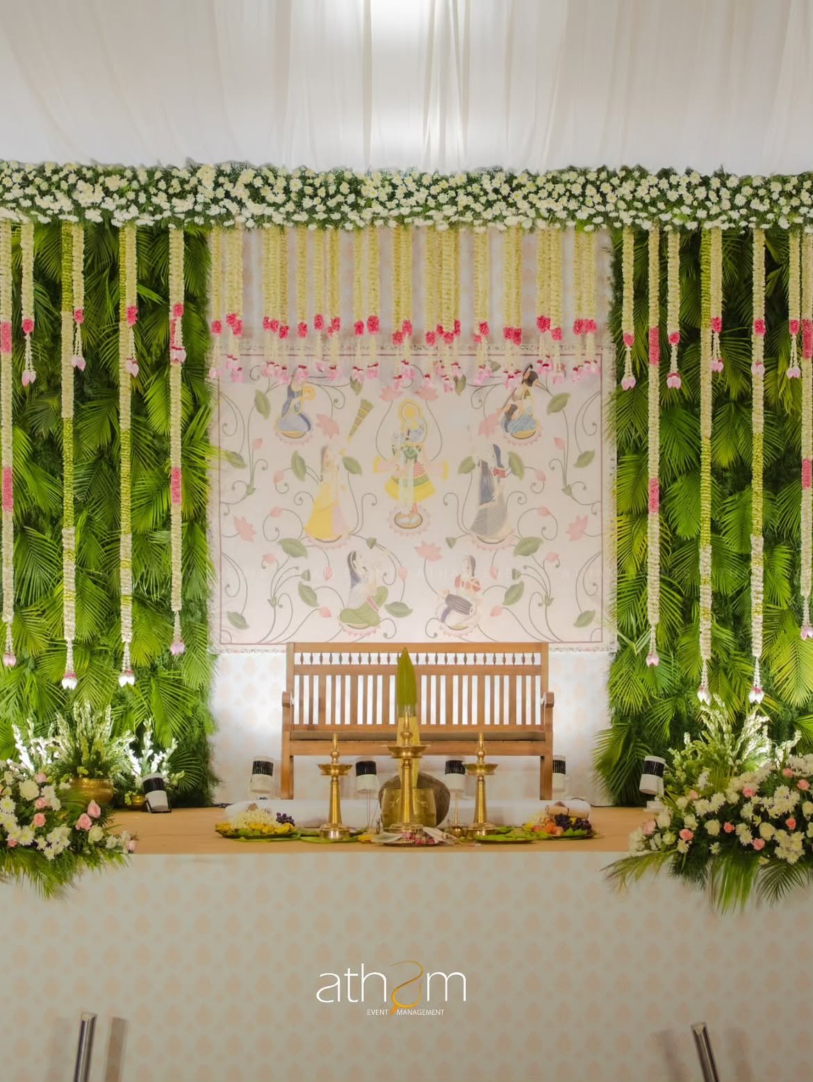 Traditional floral mandap stage backdrop with brass nilavilakku and Pichwai art